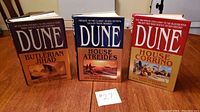 Full set of 3 large hardcover Dune novels with dust jackets: The Butlerian Jihad, House Atreides, House Corrino shown upright on a table with a label #27.