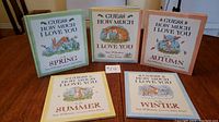 Five hardcover books displayed: 'Guess How Much I Love You', plus Spring, Summer, Autumn, Winter themed editions. Books in excellent condition with colorful illustrated covers.