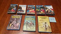 Photo showing eight Hardy Boys cassette tape books with illustrated covers arranged on a wooden surface.