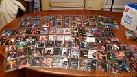 Wide shot displaying approximately 100 Batman-themed trading cards laid out across a large table. Cards feature various characters with colorful imagery.