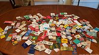 Wide view of many vintage matchbooks spread out on a wooden surface, showing various designs and colors.