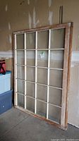 Front view of large wood sash window leaning against garage wall, showing 20 glass panes in a 5x4 grid.