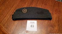 Grey felt military side cap on wooden surface, showing full hat shape and RAF badge on side.