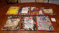7 hardcover I SPY books arranged on wooden surface, showing colorful covers and legends
