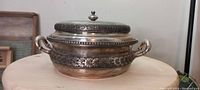 Photo showing side angle of large silver plated serving bowl with floral embossed band and lid with decorative knob.