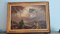 Framed oil painting showing a stormy sea with two sailors on a wooden ship and the ghostly face of a captain steering the wheel above the scene.