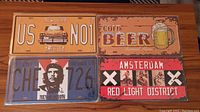 Four commemorative tin metal licence plates shown together on a wooden surface.