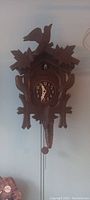 Front view of vintage wooden cuckoo clock displaying carved leaf and bird motifs, clock face, and hanging chains with weights.