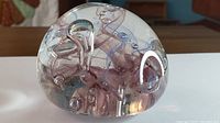 Side view of the Murano glass paperweight showing purple swirling glass with embedded bubbles inside clear glass dome.