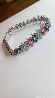 Angle view of the sterling silver bracelet showing clusters of sapphire, emerald, and ruby stones arranged in floral patterns.