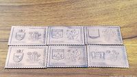 Photo showing eight solid bronze wafers arranged in two rows of four, each wafer depicting a provincial flower and coat of arms in detail.