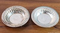 Top-down view of two sterling silver nut bowls showing fluted interiors and embossed floral border on rims