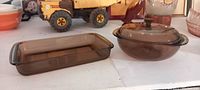 Rectangular amber/brown Pyrex baking dish and round lidded casserole dish side by side on a shelf.