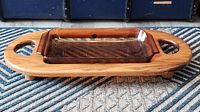 Side view of amber glass casserole dish in custom wooden serving stand with cutout handles on top of a carpet