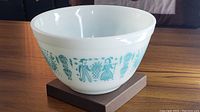Front side of vintage Pyrex Butterprint Cinderella bowl showing farmer couple and hot air balloons in teal on white milk glass.