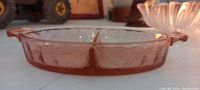 Side view of round pink glass divided serving dish with two compartments and handles, showing textured poinsettia floral pattern on sides and interior sections.