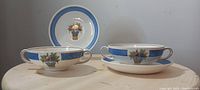 Two footed bouillon soup cups with matching saucers, blue band and basket of fruits pattern visible