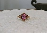 Front view of the 10k yellow gold ring with an oval pink sapphire mounted on a textured gold setting.