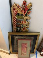 Set of beaded figures on carved wooden dragon head base with two framed artworks leaning behind on the wall