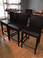 Four black bar chairs arranged inside, showing cushioned seats, backs, wooden legs, and footrests.