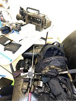 Overview of camera equipment including Sony BetaCam BVP-7x, various cameras, flashes, cases, lenses, tripod, selfie stick, and other accessories on table and couch.