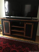 Entertainment center holding a TV and soundbar, showing dark wood and black metal sliding doors with mesh inserts, illustrating overall condition and design.