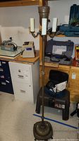 Full view of the vintage floor lamp standing next to a filing cabinet and various tools, showing its full height and three candle-like bulb holders.