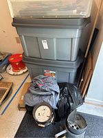 Stacked gray plastic bins with a lid and miscellaneous items like a cloth and a black plastic bag beside them.