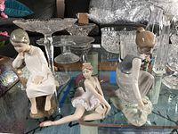Three Lladro figurines on glass table with crystal dishware in background