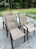 All four beige mesh stacking chairs grouped together outdoors on stone patio showing dark metal frames and rounded armrests.