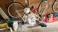 White Ross Hi-Tech Mt Hood bike with 24-inch wheels suspended upside down, beige helmet on seat, unopened helmet box nearby, surrounded by other miscellaneous items on floor.