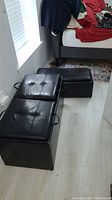 Two black storage bench ottomans placed on floor next to a bed, showing full items
