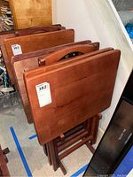 Four wooden TV trays with foldable legs stored upright in a wooden stand, showing the tops and legs of the trays.
