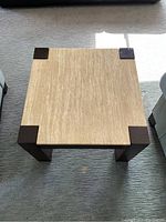 Top view of square coffee table showing beige marble surface with wood corner accents and legs.