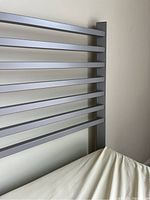Close-up of silver metal bed frame horizontal slats and top end, showing construction and material quality.
