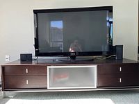 Front view of the modern wooden TV stand in dark brown finish with a large flat screen TV on top, showing two drawers on either side and a frosted glass central door.