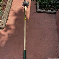 Full image of a beige wooden-handled Vigoro Roto-Edger garden tool with cutting mechanism at the end on a patio surface.
