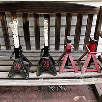 Four metal jack stands placed on wooden bench showing front view with paint chipping and red numbering on black stands.