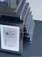 Stack of nine black IKEA Ribba picture frames sealed in plastic, view of front and sides