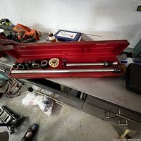 Red metal case opened showing automotive tool set inside including sockets, plastic gear tool and extension bars.
