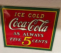 Photo of a red metal Coca-Cola sign with white and yellow text and green and yellow border.