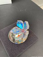 Close-up view of crystal flower ring holder showing intricate cut facets and rainbow reflections on petals and pink center, sitting on a black foam base.