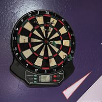 Full view of circular electronic dart board mounted on wall, showing traditional dartboard segments and digital control panel below.