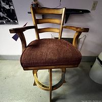 Front view of the deep red cloth seat and wooden frame swivel chair with ladder back and armrests.