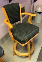 Side view showing green patterned cloth upholstery, wooden armrests, and swivel base.
