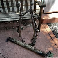 Full view of horse harness with metal hames, leather straps, and wooden hames bar on the ground beside a wooden bench.