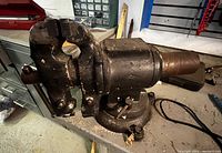 Photo of a large heavy-duty vise showing rust and missing parts on a workbench.