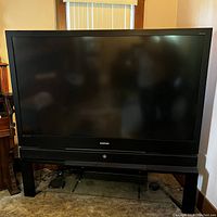 Front view of large Samsung TV with built-in soundbar and black tempered glass shelf stand.