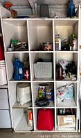 Full view of white cube shelf unit with miscellaneous household, automotive, and tool items arranged inside 12 cubbies.