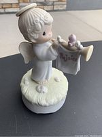 Musical angel figurine playing trumpet with 'Rejoice' banner, showing front details.